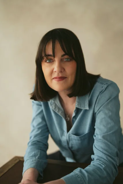 A woman in denim seated against a beige background.