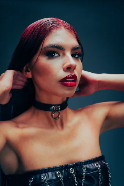 A studio portrait with a blue background, red lipstick and a black top.