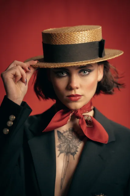 A fashion portrait with a straw hat and dark suit against a red background.