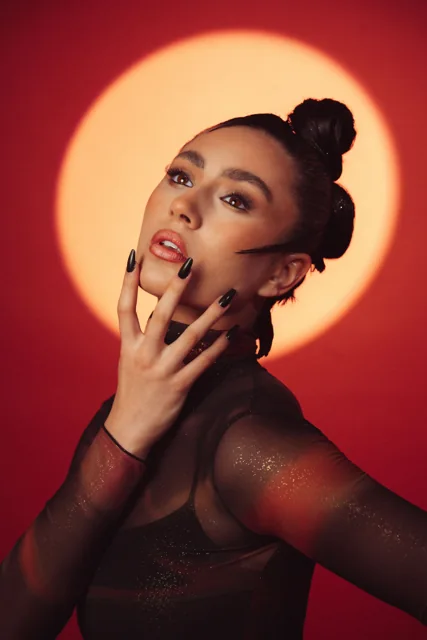 A close portrait lit in warm orange, with a circle of light behind the subject.