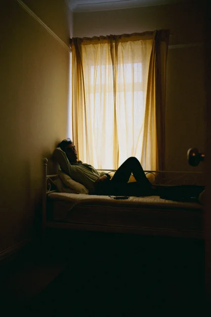 A reclining figure silhouetted beside a bright window.
