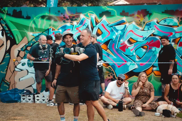 People posing in front of a colourful graffiti mural at an outdoor event.