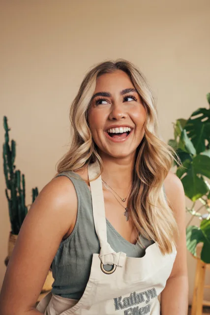 A smiling woman photographed in a plant-filled interior.