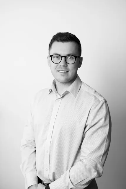 A black and white headshot of a man wearing glasses.